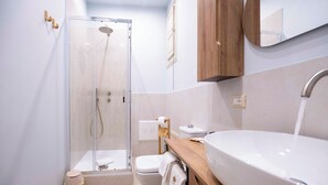 Bagno con doccia vetrata, toilette, lavabo e specchio.