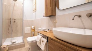 Un bagno moderno con doccia vetro, un ampio lavabo bianco, mobile contenitore in legno e specchio sopra il lavabo.