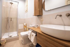 Ett modernt badrum med en dusch som är avskärmad med glasväggar, ett stort vitt handfat, en träinredd tvättställskommod och en spegel ovanför handfatet.