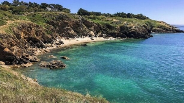 Een kustlandschap met helder turquoise water, rotsachtige kliffen en een zandstrand.