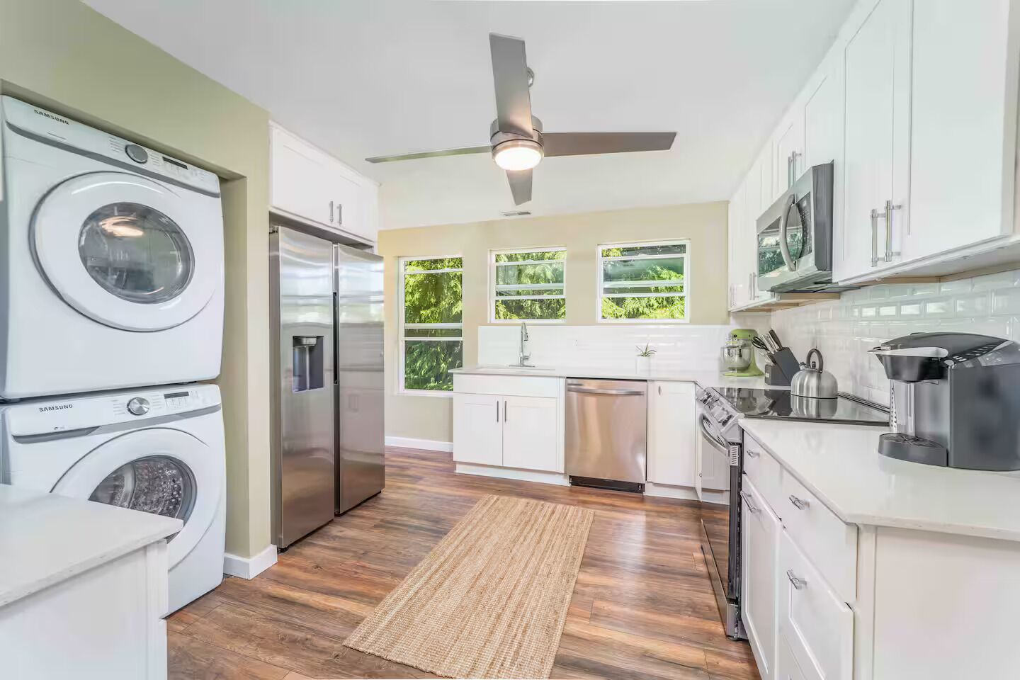 A modern kitchen with built-in appliances, a ceiling fan, and large windows offering views of greenery.