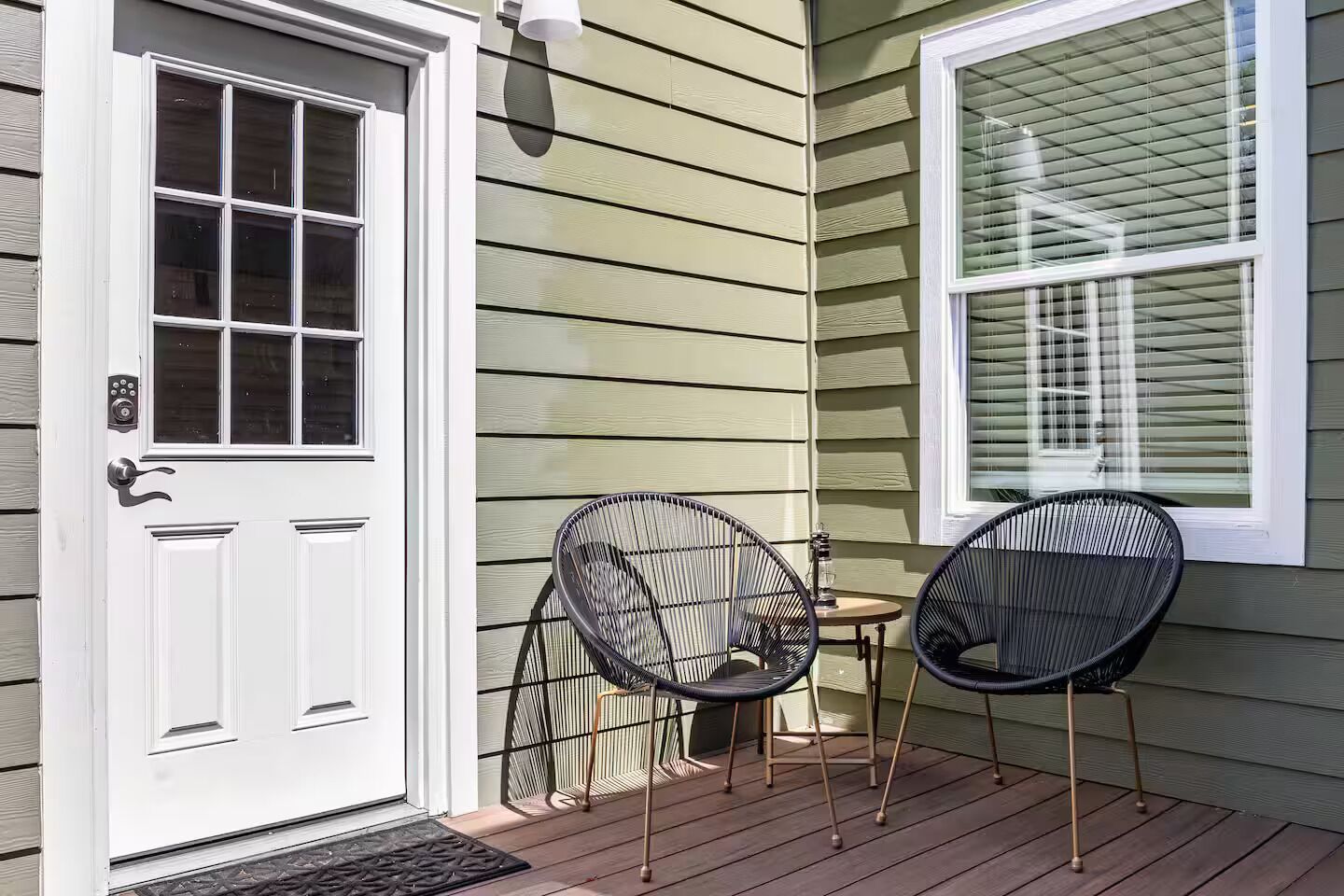 A front door with a keypad lock, two black wicker chairs, a small table, and a window with blinds.