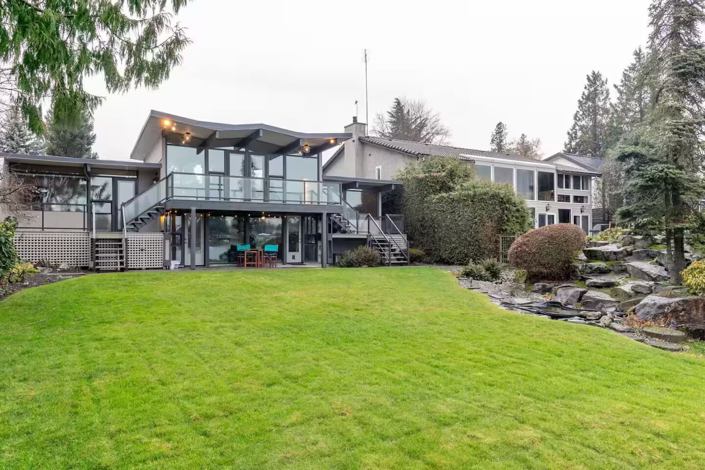 Een modern herenhuis met een overdekt terras, een verzorgd gazon en een tuin met rotsen.