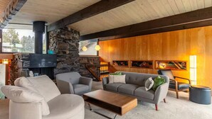 A cozy living room with a stone fireplace, wooden beams, a gray sofa, and a coffee table. - Seattle Lake Front Oasis (SeaTac)