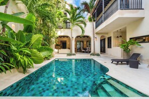 Une piscine à motifs à carreaux, entourée d’une végétation luxuriante et dotée d’un balcon avec une balustrade.