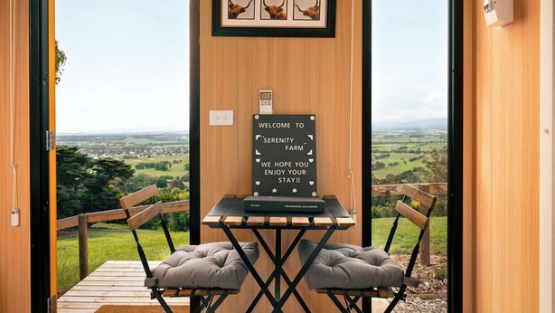 Een kamer met houten frame en uitzicht op het landschap, een welkomstbord, een tafel met stoel en een bank.