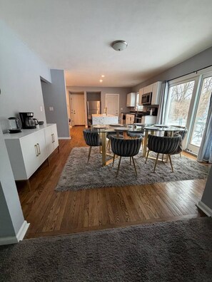 A modern kitchen with a dining area, wooden flooring, and a view through large windows.