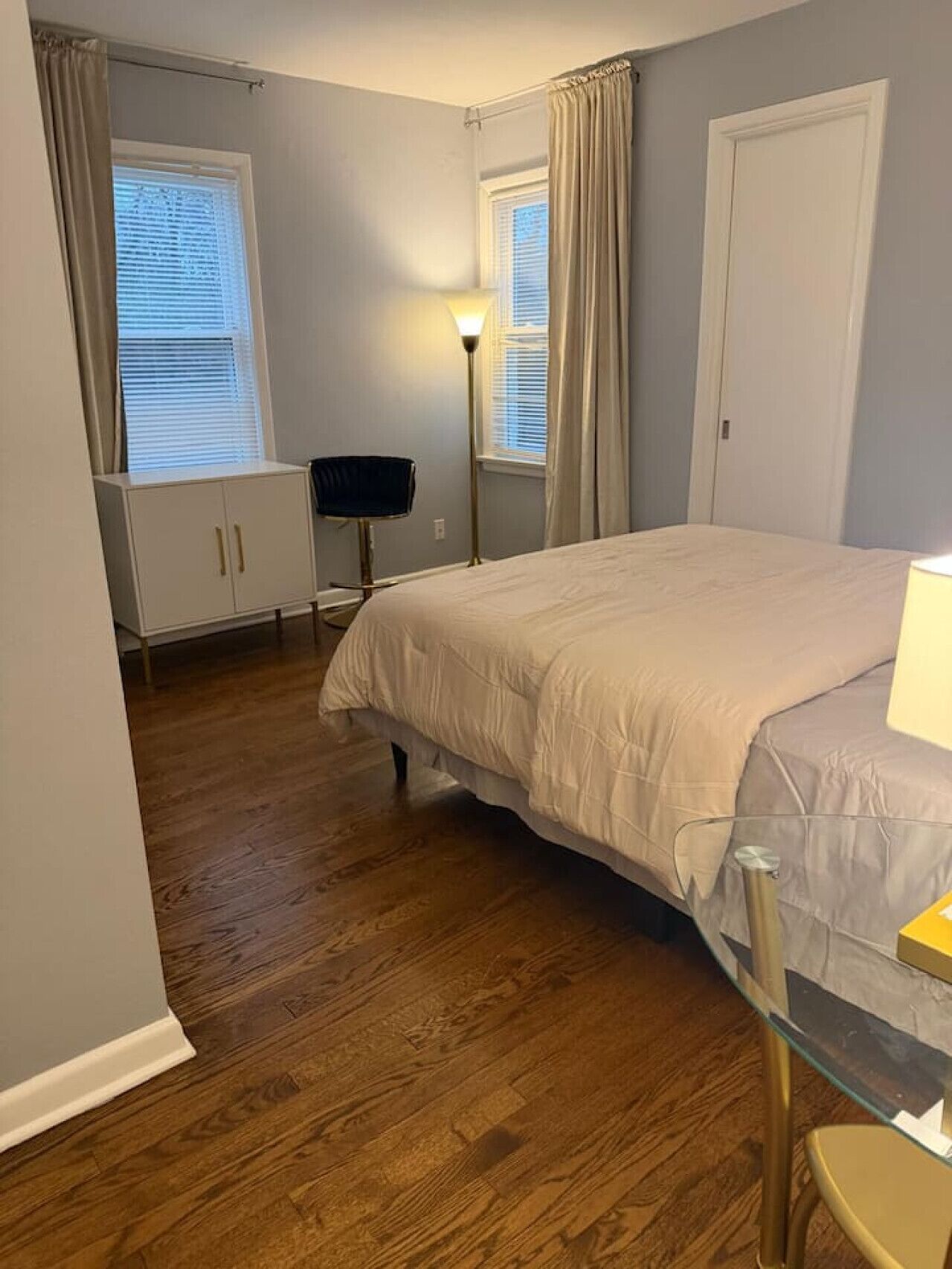A bedroom with a bed, a wardrobe, a desk, a chair, and a floor lamp.