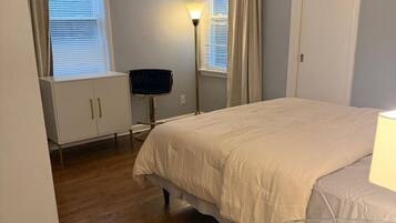 A bedroom with a bed, a wardrobe, a desk, a chair, and a floor lamp.