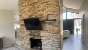A stone fireplace with a flat-screen TV, a bench, and a view of a bedroom.