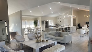 A modern living room with a sofa, chairs, a coffee table, and a kitchen in the background.