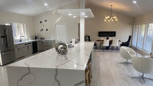 A modern kitchen with a marble island, stainless steel appliances, and a dining area with white chairs.