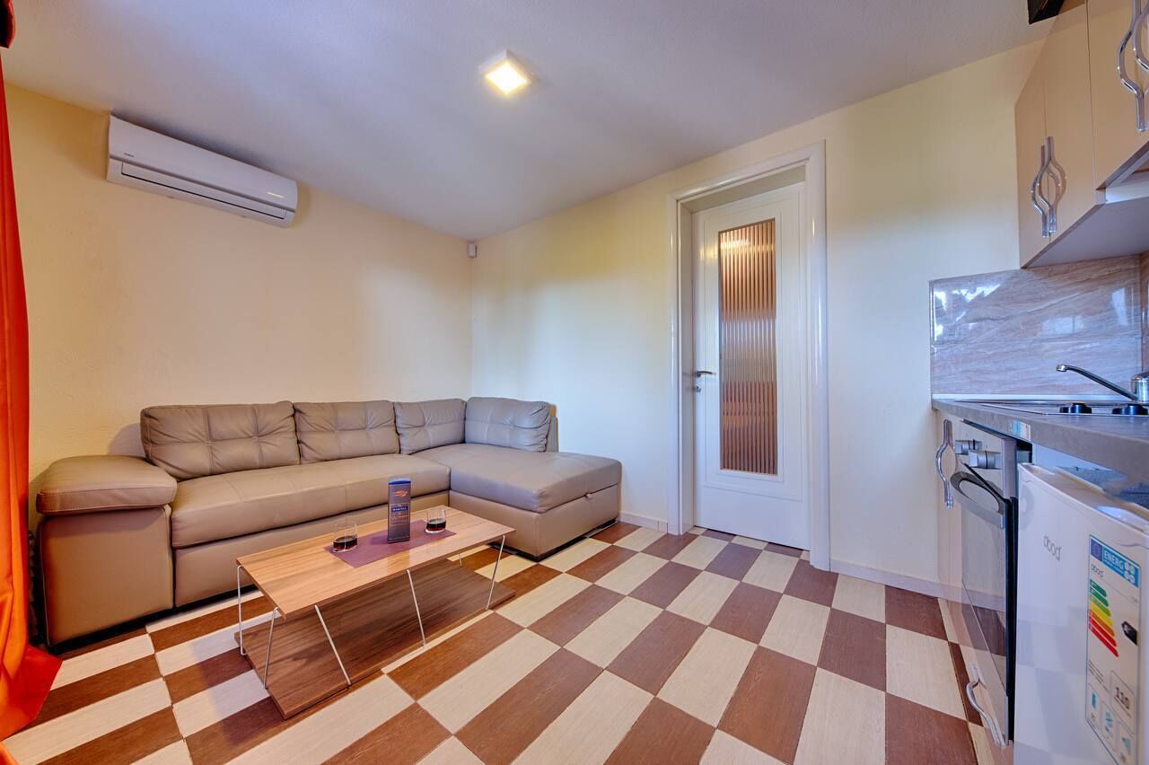 Un espacio habitable compacto con un sofá, una mesita de centro, una zona de cocina con refrigerador y un piso a cuadros.