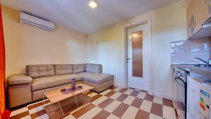 A compact living space with a sofa, a coffee table, a kitchen area with a refrigerator, and a checkered floor. - Apartman ZIS 1L (Opština Bar)