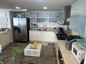 Eine moderne Küche mit einem Edelstahl-Kühlschrank, einer Mikrowelle und einem Herd. Es gibt ein Waschbecken mit Armatur und eine kleine Kücheninsel mit Kerze und Zitronen. Die Küche verfügt über weiße Schränke und eine geflieste Spritzschutzwand.