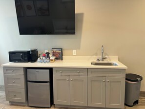 A kitchenette with a microwave, coffee maker, water bottles, a trash can, and a sink.