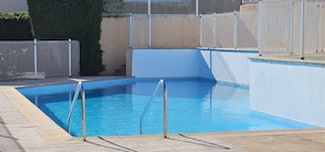 Ein rechteckiger Pool mit einer gefliesten Terrasse, einer Metallleiter und einem weißen Zaun darum.