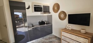 Eine kompakte Küche mit Mikrowelle, Toaster und Wasserkocher, einem Flachbildfernseher und einem Holztischchen mit Dekoration.
