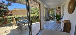 A room with a sliding glass door leading to a patio, a dining table with chairs, a potted plant, and a wooden cabinet. - Appartement 4 personnes, climatisé, Wifi, parking, terrasse et piscine ! (Cavalaire-sur-Mer)