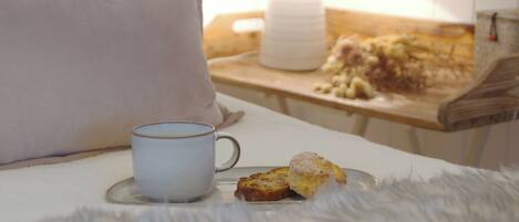 A cozy bedroom with a bed, a bedside table with a lamp, a cup, and a plate with food.