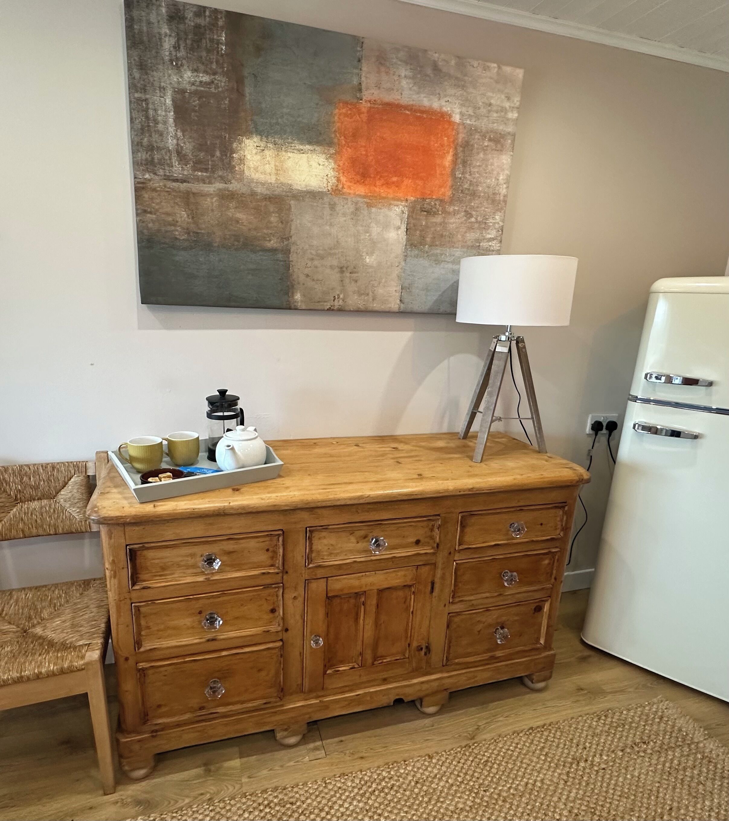 A wooden dresser with drawers, a lamp, and a tray with cups and a teapot.