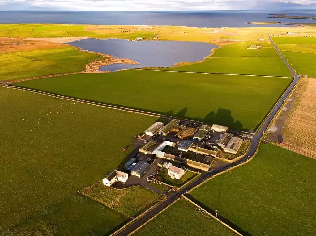 An aerial view of a large industrial complex with multiple buildings, roads, and green fields.