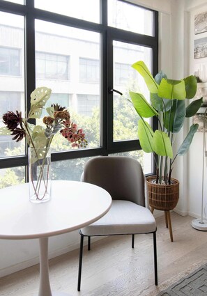 Ein Zimmer mit großem Fenster, einem weißen Tisch, einem grauen Stuhl und zwei Zimmerpflanzen.