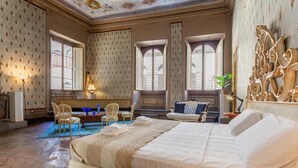 Et hotelværelse med en stor seng, et siddeområde med stole, et lille bord og et vindue med skodder.