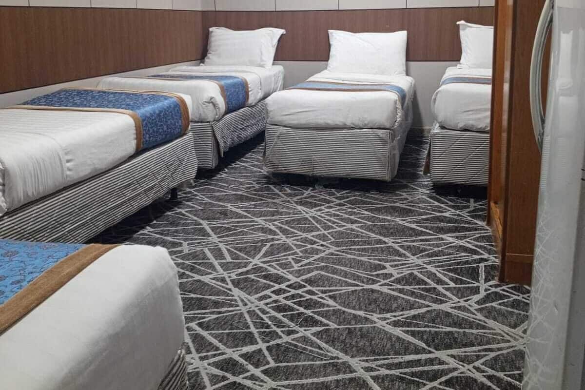 Een hotelkamer met drie bedden, een kamerbreed tapijt met dessin en een koelkast.