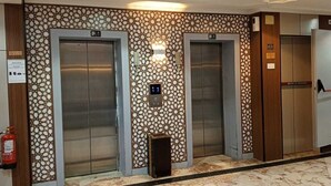 Un hall d’entrée doté de deux ascenseurs, d’un extincteur et d’un motif décoratif sur le mur.