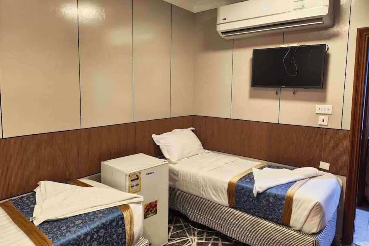 Een kleine hotelkamer met twee bedden, een kitchenette, een airconditioner en een televisie die aan de muur is bevestigd.