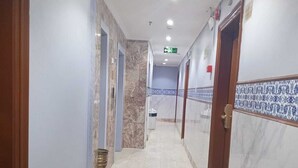 Un couloir doté d’un sol en marbre, de murs aux motifs bleus et blancs, et de portes donnant sur différentes pièces.