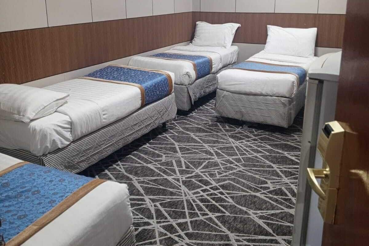 Een hotelkamer met vier enkele bedden, een kamerbreed tapijt met dessin en houten paneelwanden.