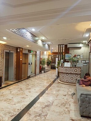 Een hotellobby met marmeren vloer, liften, een receptiebalie en een zithoek.