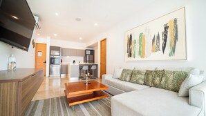 A modern living room with a sofa, a coffee table, and a TV. There is a kitchen in the background with a dining area. - 2 BR Condo with Rooftop Pool - Sasha II (Playa del Carmen)