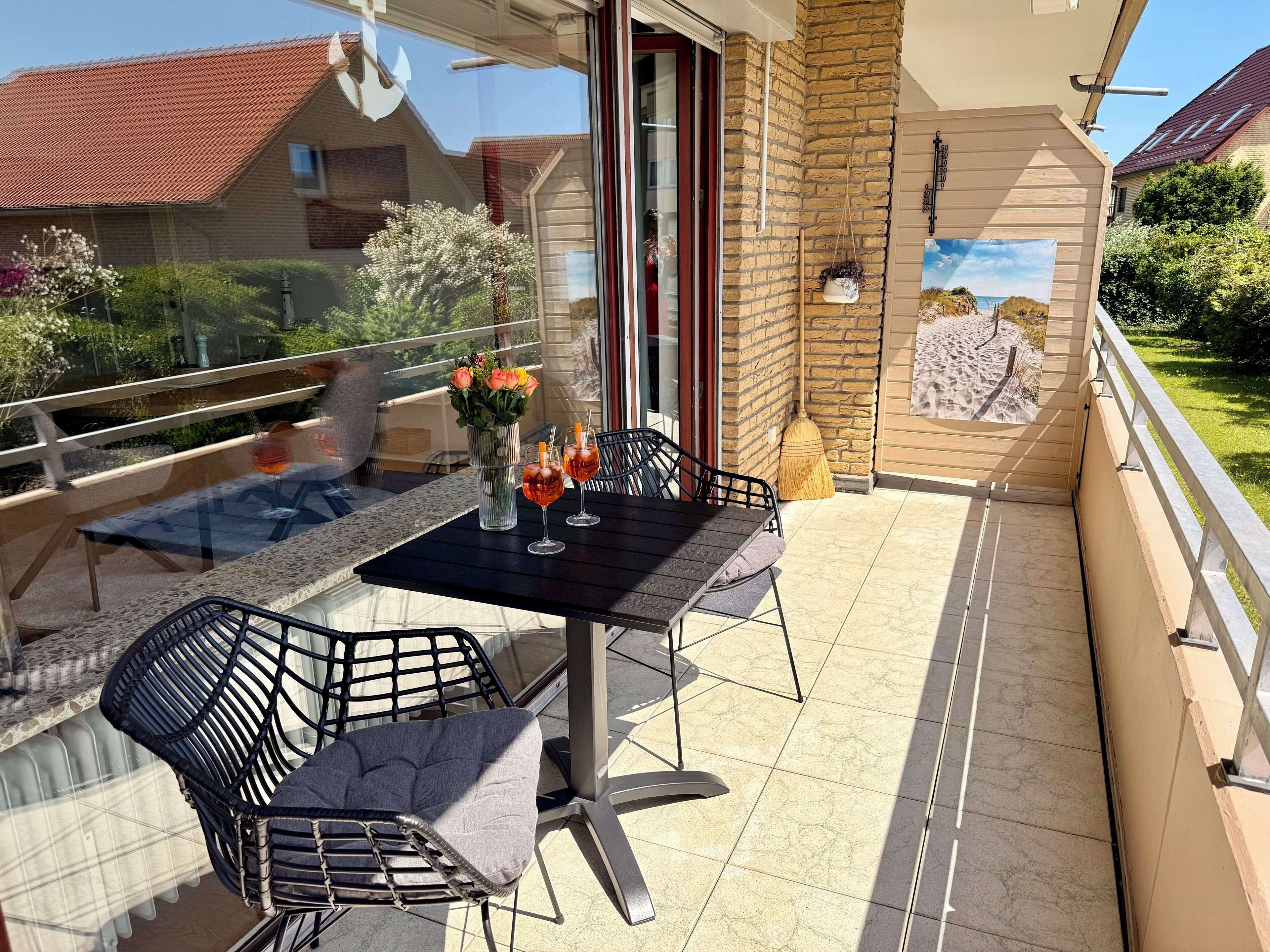 A balcony with a table, two chairs, a vase with flowers, and a painting on the wall.