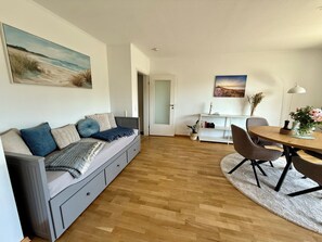 A modern living room with a sofa, a dining table, and a bookshelf. - Vacation apartment Grömitz - outstanding location - dyke.promenade.Baltic Sea.beach.town. (Grömitz)