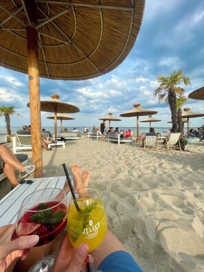 A beach with umbrellas and lounge chairs, a clear sky, and a person holding a drink. - Vacation apartment Grömitz - outstanding location - dyke.promenade.Baltic Sea.beach.town. (Grömitz)