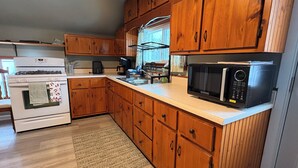 A compact kitchen with wooden cabinets, a white stove, a microwave, and a coffee maker. - 15 Min to Lansing • 2BR • In-Unit Washer & Dryer (Grand Ledge)