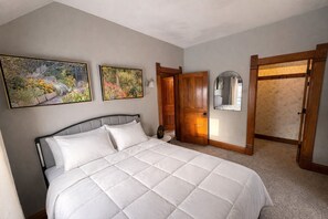 A bedroom with a large bed, wooden doors, and two framed floral paintings on the wall. - 15 Min to Lansing • 2BR • In-Unit Washer & Dryer (Grand Ledge)