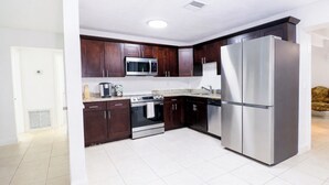 A modern kitchen with dark wooden cabinets, stainless steel appliances, and a white tiled floor. - 5BR West Palm Beach Getaway with Fenced Yard, Pets Welcome (West Palm Beach)