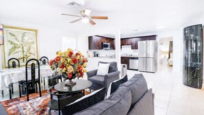 A modern living room with a grey sofa, a round coffee table, and a floral centerpiece. A dining area with a table and chairs is visible in the background. - 5BR West Palm Beach Getaway with Fenced Yard, Pets Welcome (West Palm Beach)