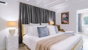 A bedroom with a bed, bedside tables, a lamp, a chair, a painting, and a window with curtains. - 5BR West Palm Beach Getaway with Fenced Yard, Pets Welcome (West Palm Beach)