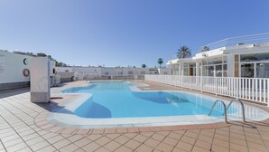 Ein Schwimmbecken mit gefliestem Sonnendeck, einem Rettungsring und einem weißen Zaun, der das Areal umgibt.