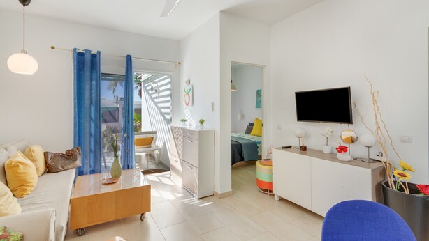 Ein modernes Wohnzimmer mit Sofa, Couchtisch, Fernseher und einem Essbereich mit Tisch und Stühlen.