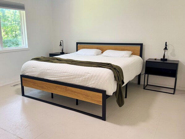 Un dormitorio moderno con estructura de cama de madera, ropa de cama blanca y dos mesitas de noche con lámparas.