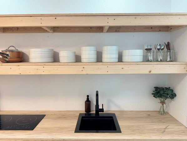 Een keuken met een zwart spoelbak, een fornuis en planken met witte bakjes en glazen potten.