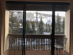 A balcony with two metal chairs, a view of a snowy mountain landscape, and a building in the background. - Cozy 1-bedroom condo A204 with 2 sofabeds in quaint Vail Village with AC comfort (Vail)