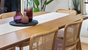 Un comedor con una mesa de madera, sillas de mimbre y un jarrón con plantas verdes.