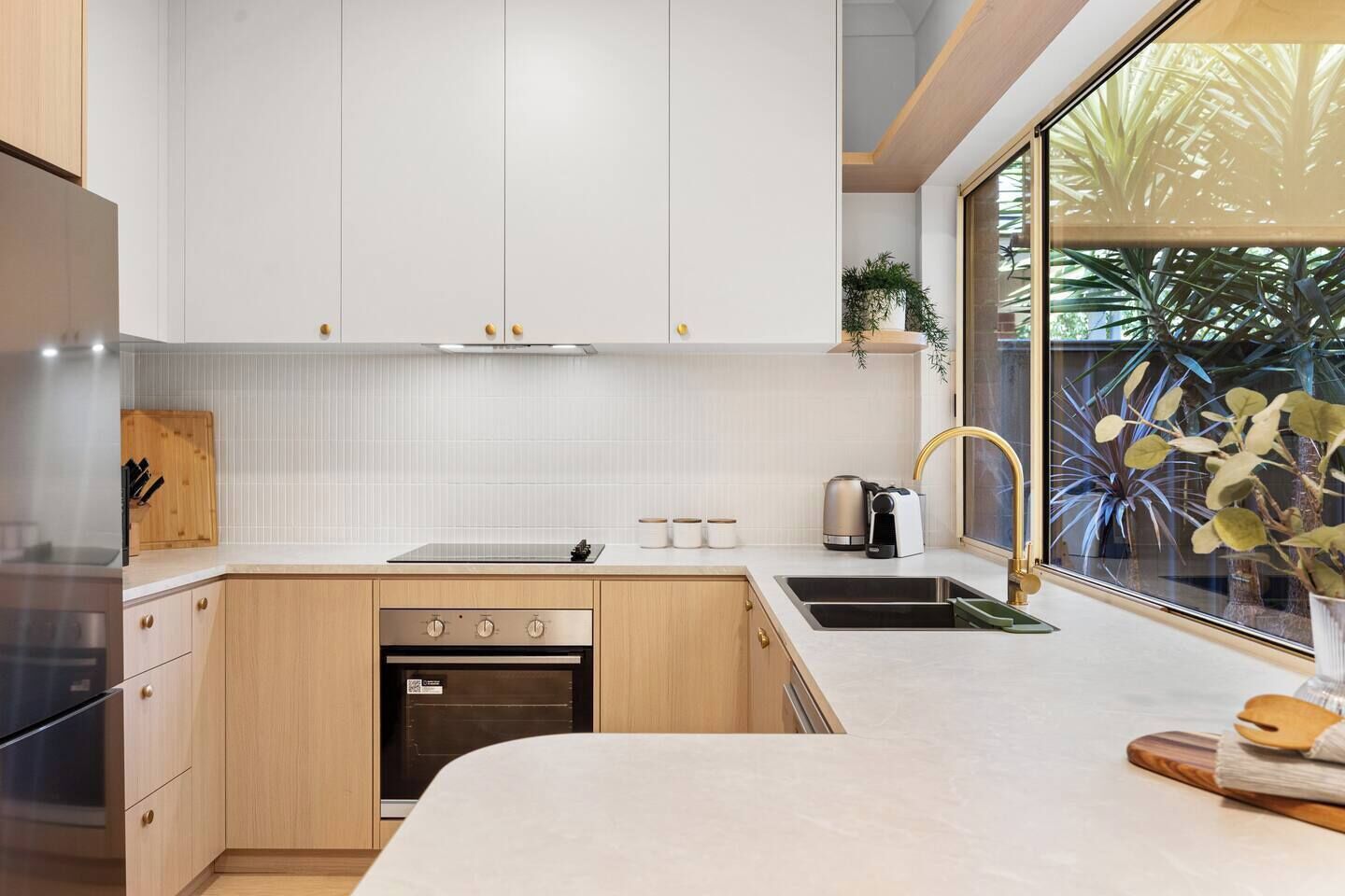 A modern kitchen with white cabinetry, a built-in oven, a sink, and a window with a view of greenery.